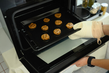 Baker wearing an oven mitt placing a tray of chocolate chip cookie dough into the oven