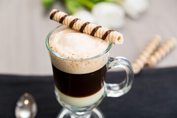 Coffee Bombon in a glass on the table with a waffle tube