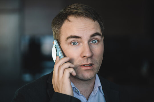 The call is causing confusion on the face. A businessman communicates on a smartphone in the dark at night. perplexed young man dressed in a shirt, who is something unpleasant by phone