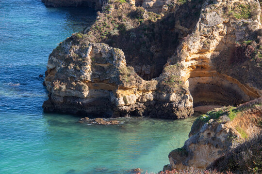 Coastal rock formations and blue sea under clear skies in Algarve, South of Portugal