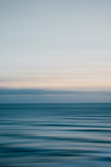 A tranquil ocean scene with a clear blue sky in the background. The water appears calm and still, with no visible waves or ripples. The sky is a light blue color