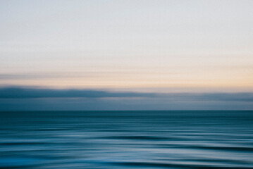 Obraz premium A calm ocean with a cloudy sky in the background. The sky is a mix of blue and white, giving the impression of a peaceful and serene scene