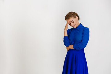 Woman in a blue dress on a white background bowed her head down with her hand covering her arm