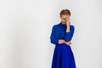 Woman in a blue dress on a white background half her face covered with her hand