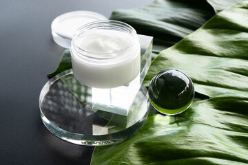 Cosmetics are artistically arranged with cream and a glass orb on green tropical leaves.