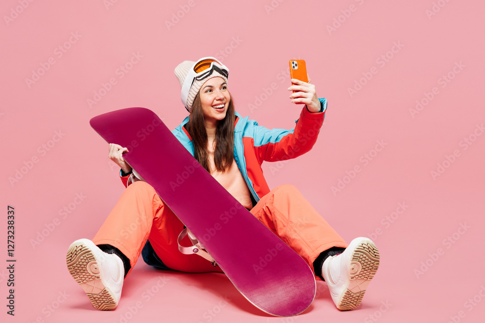 Poster Full body young woman wear blue jacket ski goggles mask spend weekend winter season in mountains sit with snowboard do selfie shot on mobile cell phone isolated on plain pink background Hobby concept