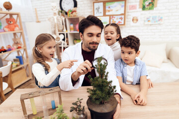 Children together with the teacher look through a magnifying glass on a plant.