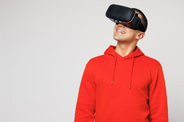 Young smiling happy middle eastern man he wears red hoody casual clothes watching in vr headset pc gadget play video game isolated on plain solid white background studio portrait. Lifestyle concept.