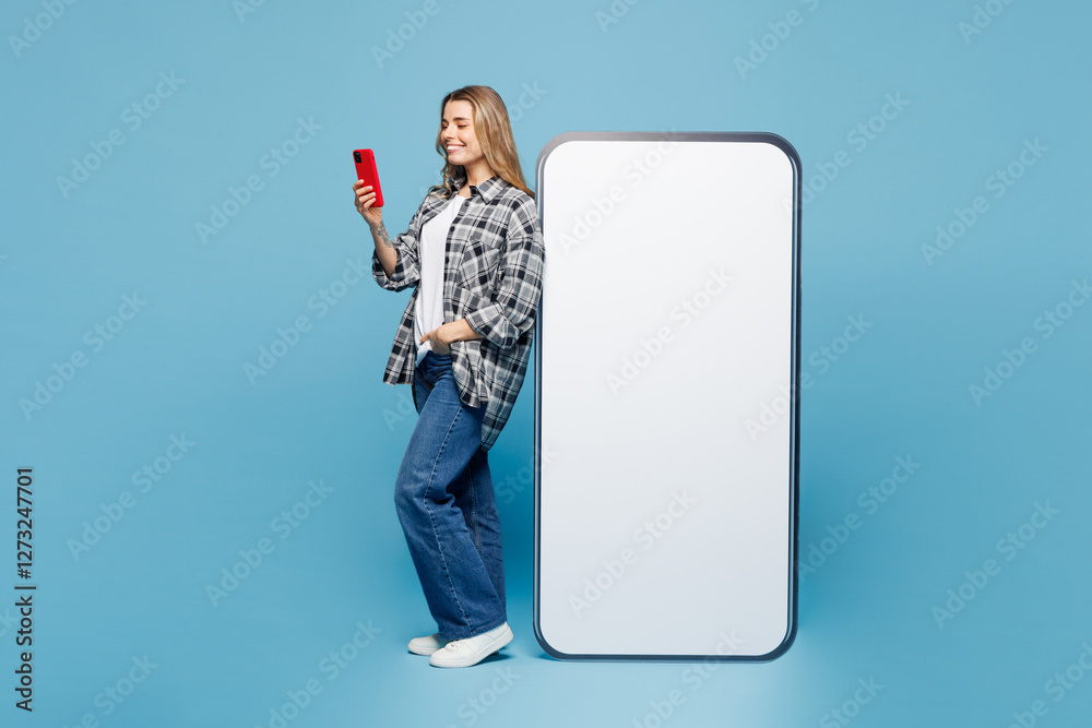 Sticker Full body side view young smiling happy woman she wears checkered grey shirt casual clothes big huge blank screen mobile cell phone with area using smartphone isolated on plain pastel blue background.