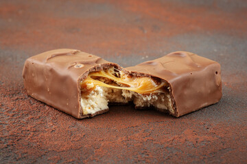Closeup of chocolate bar with peanuts, caramel and nougat, brown background