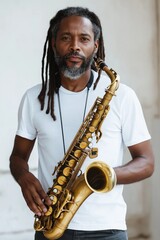 Fototapeta premium A man with dreadlocks is holding a saxophone. He is wearing a white shirt and he is in a serious or focused mood