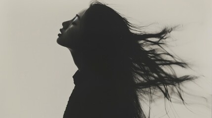 Fototapeta premium A blurred black and white photograph of the silhouette of an Asian woman with long hair, standing in front of a plain background