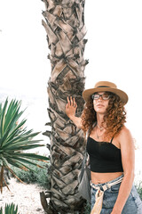 A young woman in a stylish hat stands near tall palm trees on a sunny day. A young tourist walking on the streets of Europe.