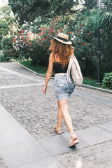Happy woman with straw hat and backpack enjoying summer walks. A young tourist walking on the streets of Europe.