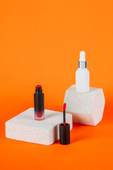 White tube and red spray on light white podiums. White blank unbranded flacons with cosmetology products. Professional concept of skin care on orange background.