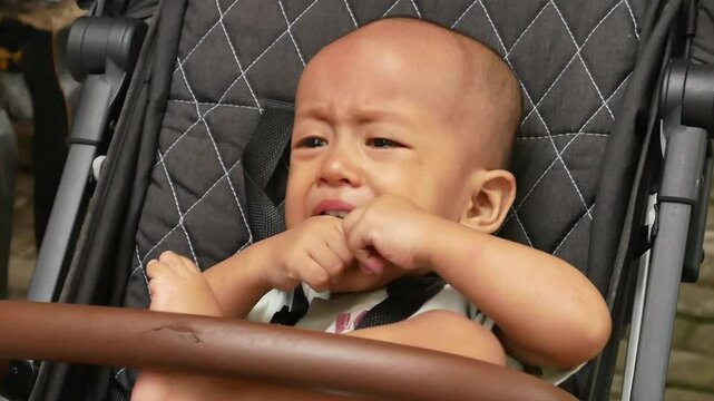 Asian male toddler cries and babbles because his desires are not fulfilled by crying and biting his fingers and toes. Toddler babbling in a stroller.