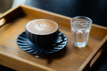 Side view of hot latte coffee with latte art in a black cup on black wooden table