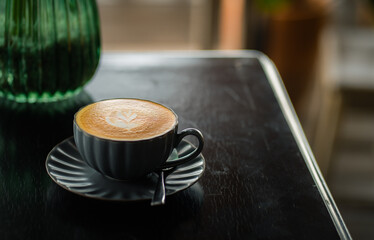 Side view of hot latte coffee with latte art in a black cup on black wooden table
