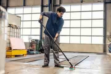 Neat multicultural industry worker with broom in hands cleaning around facility.