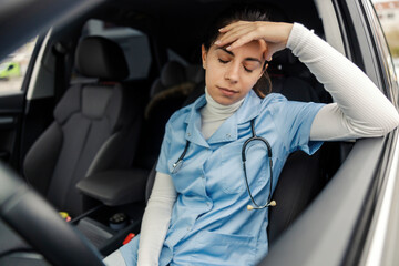 Tired female doctor sitting in her car and having headache after night shift.