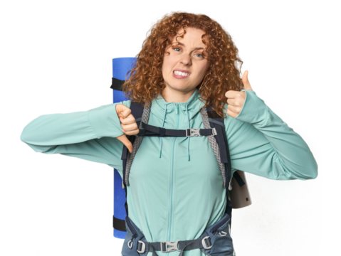 Young Caucasian redhead ready for hiking showing thumbs up and thumbs down, difficult choose concept