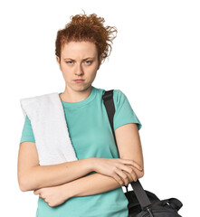 Young Caucasian redhead with gym gear frowning face in displeasure, keeps arms folded.