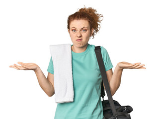 Young Caucasian redhead with gym gear doubting and shrugging shoulders in questioning gesture.