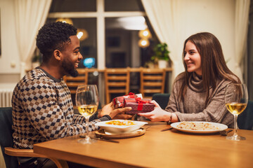 Two friends are having dinner at restaurant. They are exchanging gifts.