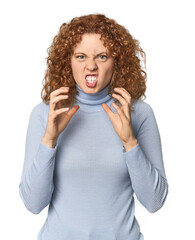 Young Caucasian redhead woman upset screaming with tense hands.