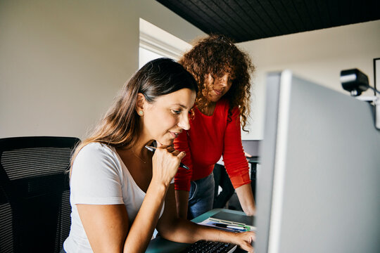 Two diverse Women Collaborating On A Project In A Modern Office Setting. They look focused on a laptop