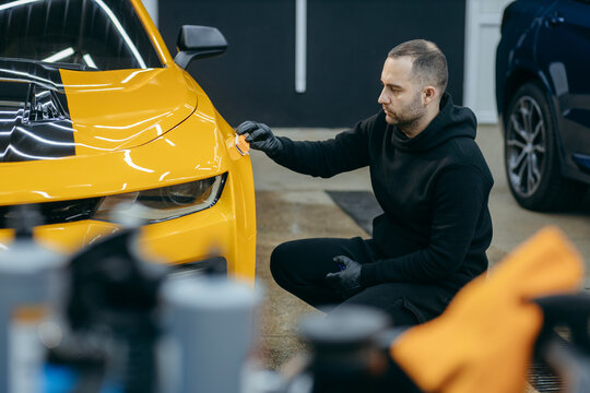 Car detailing worker applying ceramic car coating on yellow car at workshop