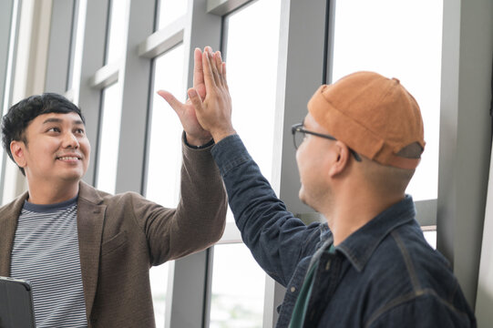Asian male businessman Tag a friend's hand happy smile Holding a tablet, talking about analytics, innovation, and collaboration. Online business, sales techniques, strategic planning