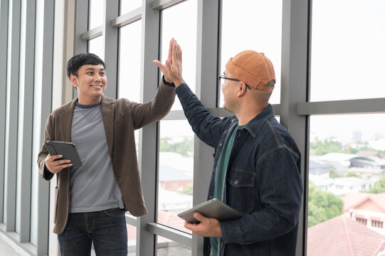 Asian male businessman Tag a friend's hand happy smile Holding a tablet, talking about analytics, innovation, and collaboration. Online business, sales techniques, strategic planning