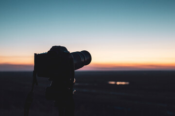 Obraz premium camera at sunset on tripod shooting beautiful sunny horizon with long exposure, background blurred with bokeh effect