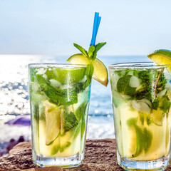 Cocktail mojito with ice and lemon in two glasses on the background of the ocean closeup