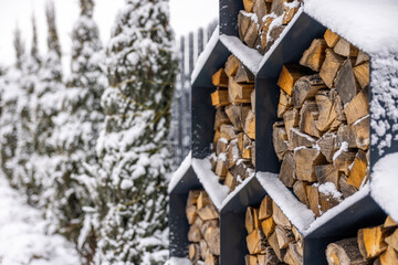 Close-up of stacked firewood in hexagonal metal storage covered with snow in a winter backyard.