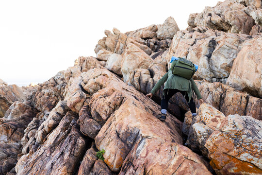 Biracial female hiker climbing rocky terrain amidst nature, copy space
