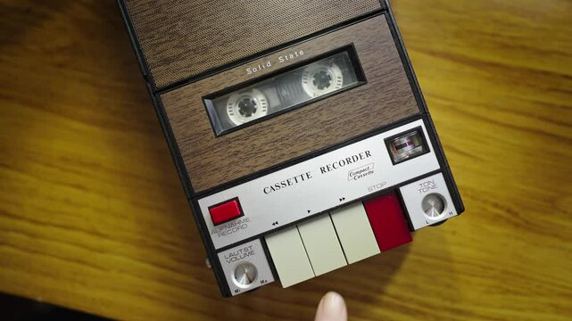 Hand inserts cassette tape into retro portable recorder and presses play button