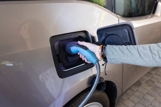 Charging electric car, female hand holding plug and connecting it to the vehicle