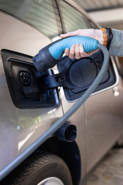 Charging electric car, woman holding plug and connecting it to the vehicle