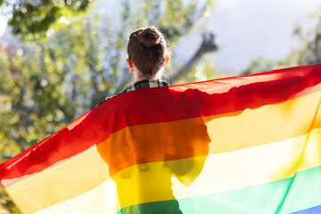 Woman holding rainbow flag draped over shoulders, standing outside