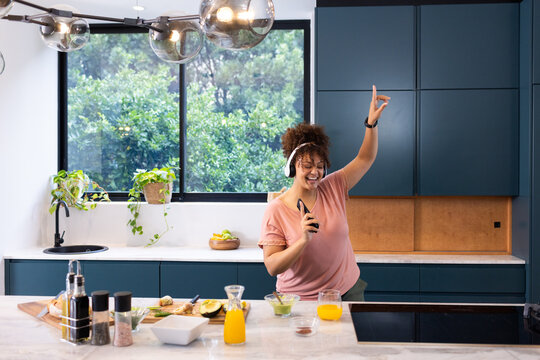 Dancing in kitchen, woman wearing headphones and holding smartphone, enjoying music, at home, at hom