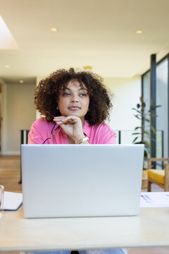 Working on laptop, woman in pink shirt thinking and holding pen, copy space, at home
