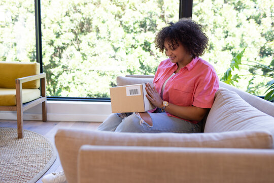 Sitting on couch, woman opening package and smiling, enjoying her delivery, at home