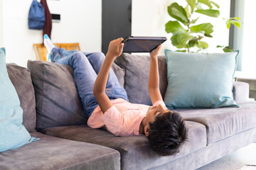 Lying on couch, Indian boy using tablet for entertainment at home