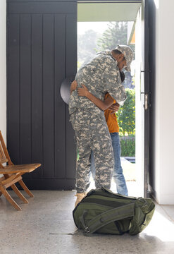 Welcoming indian father in military uniform, young son hugging him, green duffel bag nearby