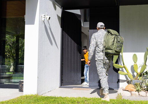 Returning home, soldier in uniform with backpack greeted by young son at door, copy space