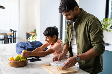 Packing lunch, indian father and son preparing for school in kitchen together