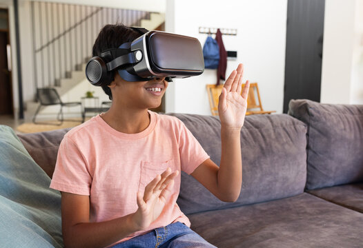 Using VR headset, Indian boy sitting on couch and playing virtual reality game - Powered by Adobe
