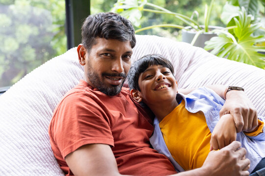 Indian father and young son relaxing on couch, smiling and enjoying time together